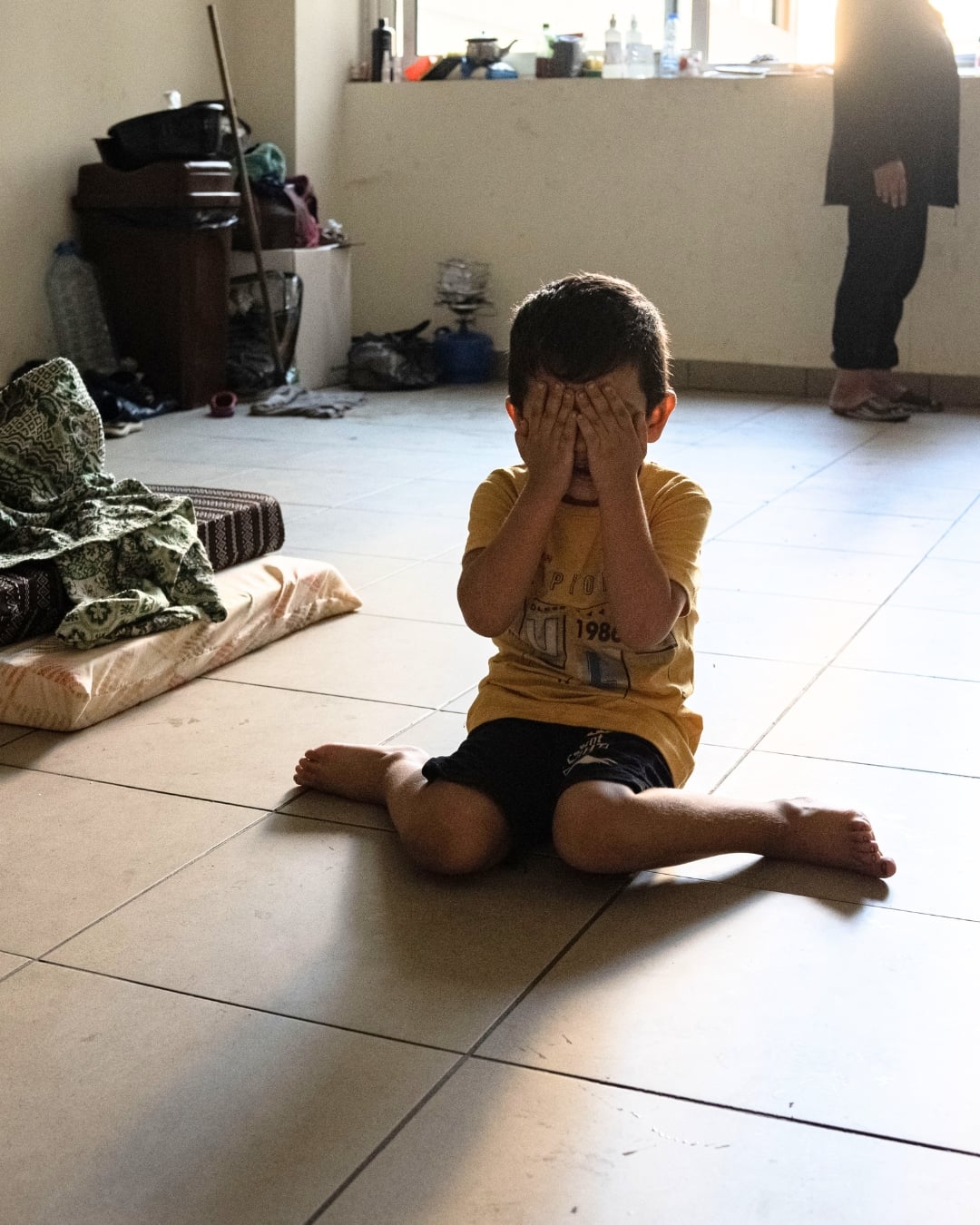 A displaced Lebanese boy covers his face with his hands as he sits on the floor of the school classroom where he and his family are living in Beirut, Lebanon, after being forced to flee their home.