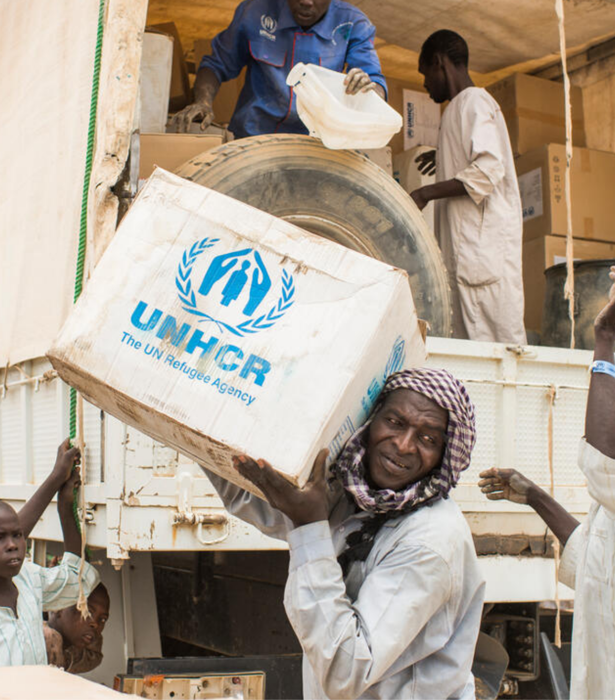 People unload UNHCR relief boxes from a truck during a humanitarian aid distribution.