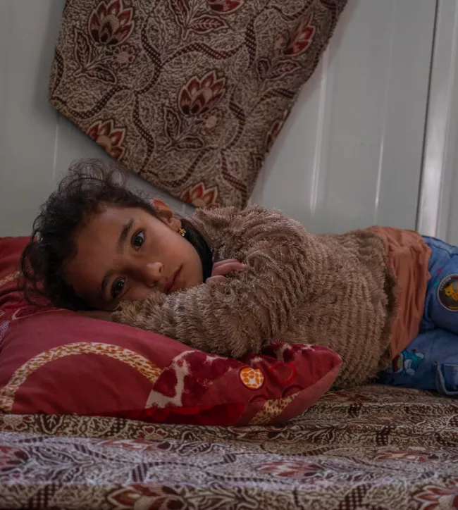 Seven-year-old Retaj AlMaslamani lays on a mattress on the ground inside a shelter in Zaatari refugee camp in Jordan. Her grandmother Ghasiba, 57, cares for her and her two younger sisters since their parents are divorced. When it rains the shelter leaks, and her grandmother struggles to keep them warm and dry.