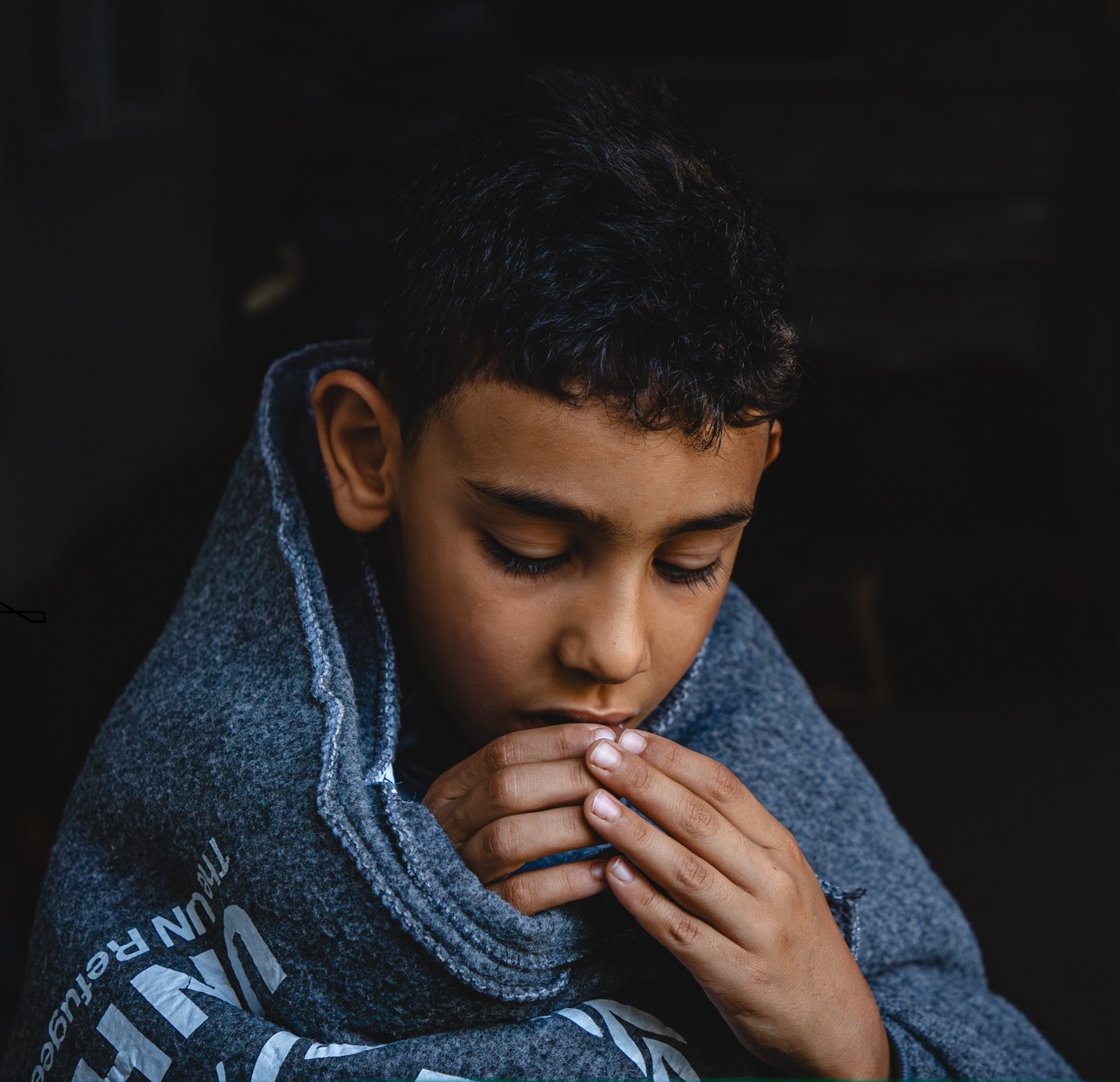 refugee boy coverd on blanket looking down