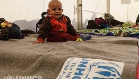 A baby sitting on UNHCR blanket.